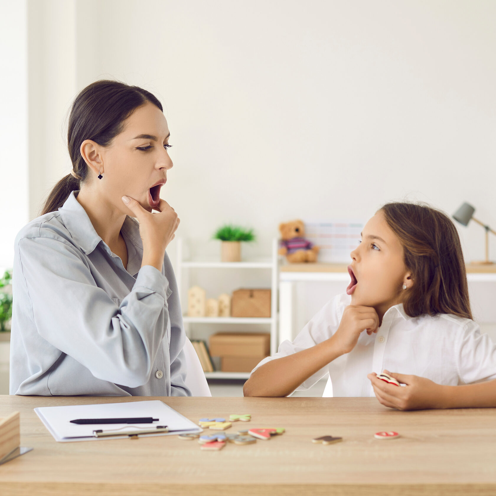 Happy child and young female speech therapist or mother doing mouth exercise, working on pronunciation problems, correcting sounds, fixing stuttering stammering impediment, and having fun together